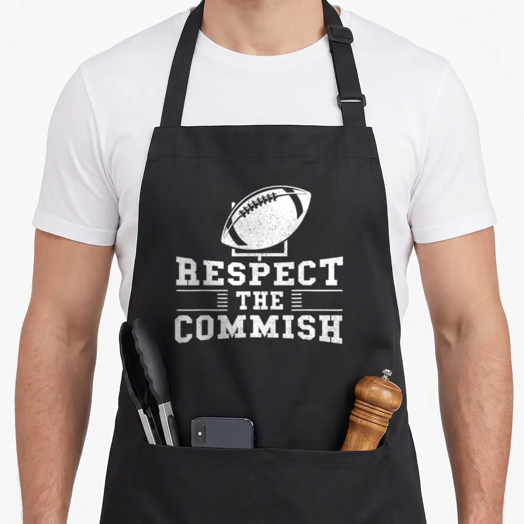 Respect football apron - White distressed text reading Respect The Commish below a football on a goalpost outline — shown on a black cotton canvas apron against a white background