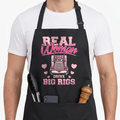 Drive truck girl apron - Pink distressed Real Woman Drive Big Rigs text with semi-truck and hearts — shown on a black cotton canvas apron against a white background