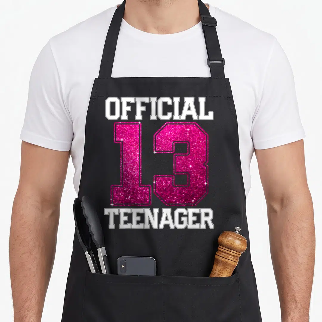Bday tween birthday apron - OFFICIAL 13 TEENAGER in pink glitter and white block letters stacked vertically — shown on a black cotton canvas apron against a white background