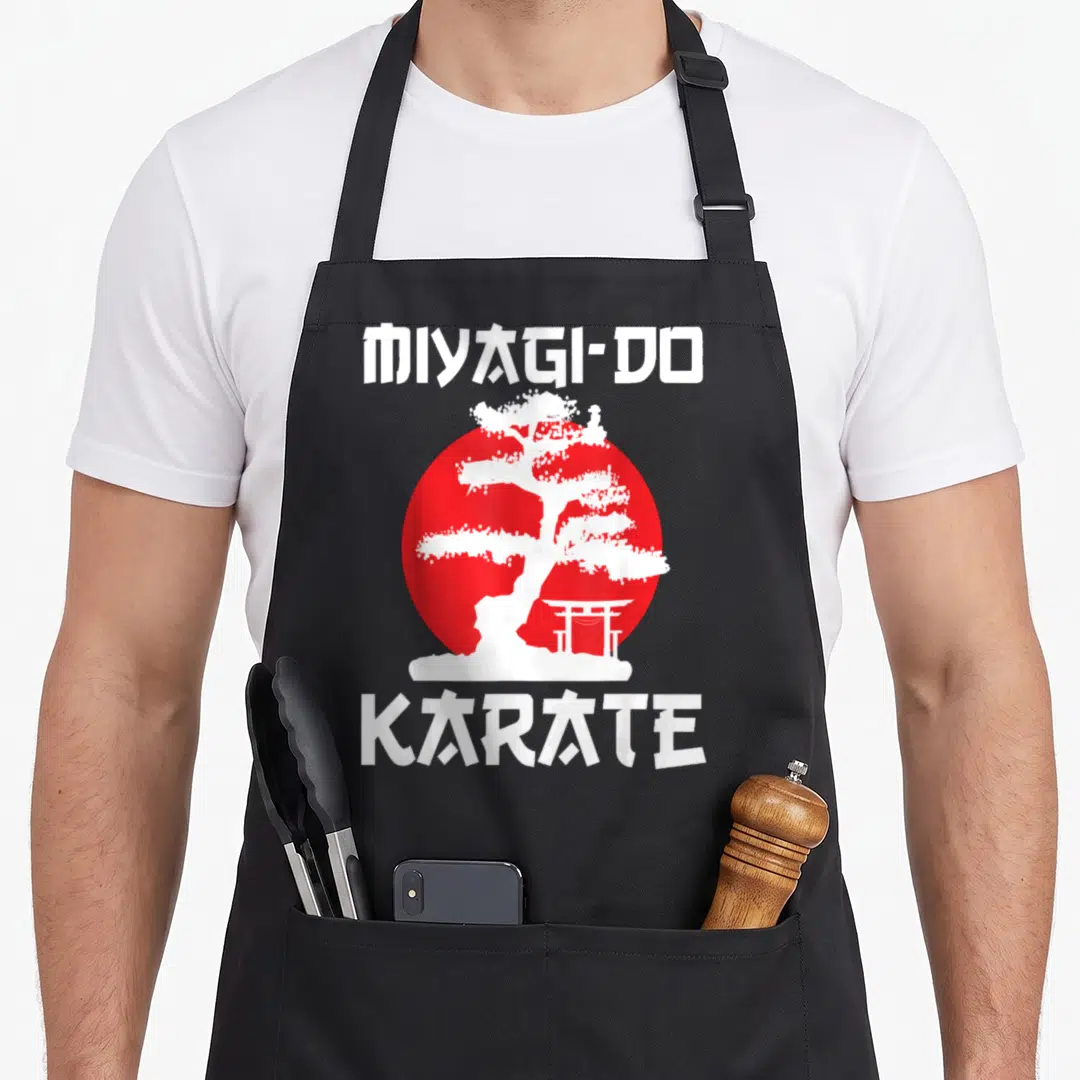 Martial tree apron - White bonsai and torii gate silhouette over a red circle with MIYAGI-DO KARATE text — shown on a black cotton canvas apron against a white background
