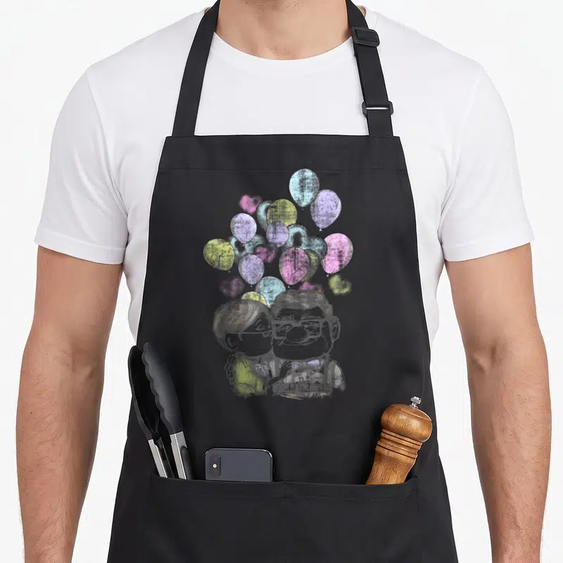 Carl valentine apron - Cartoon sketch of a couple with grey, pink, purple, yellow, and blue heart-shaped balloons — shown on a black cotton canvas apron against a white background