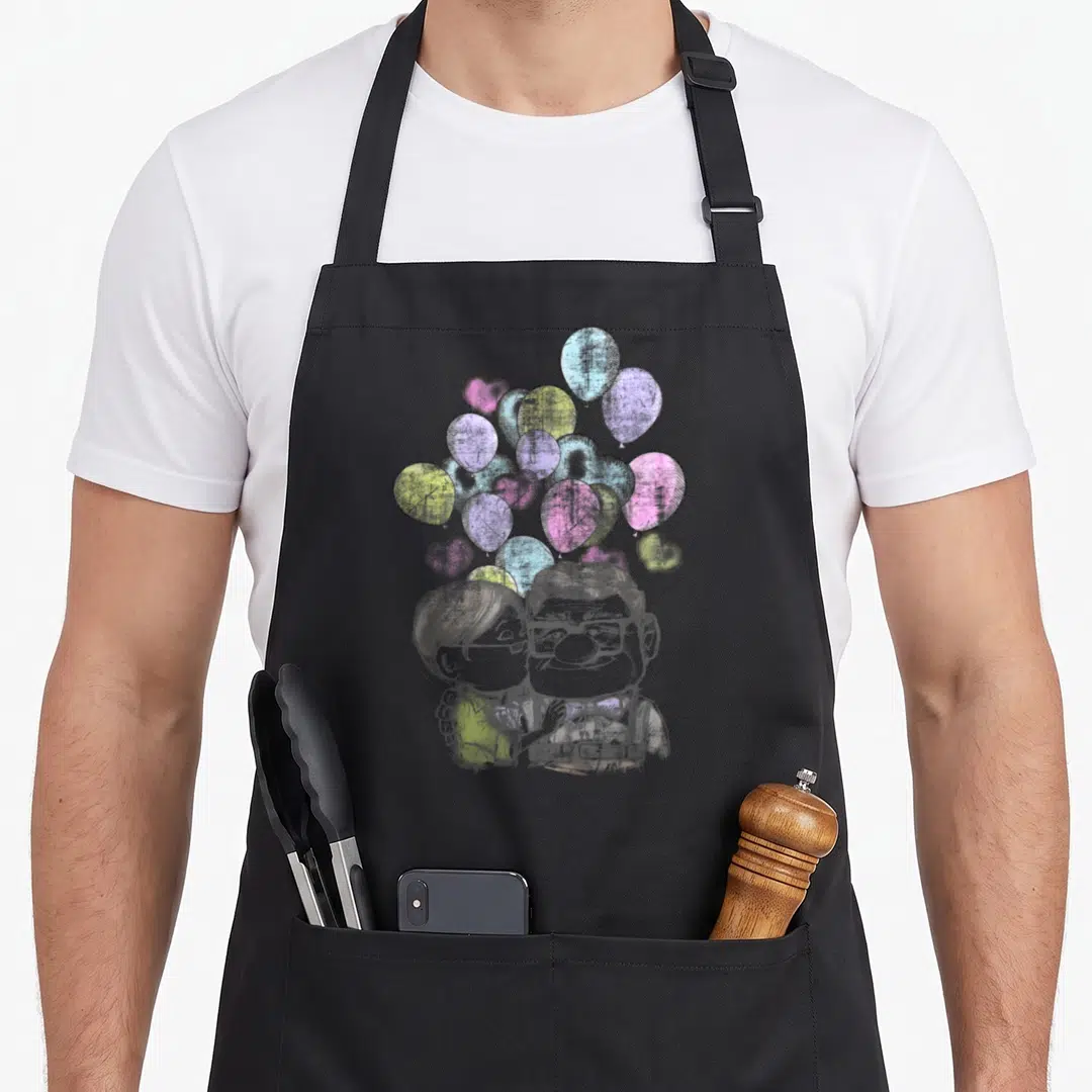 Carl valentine apron - Cartoon sketch of a couple with grey, pink, purple, yellow, and blue heart-shaped balloons — shown on a black cotton canvas apron against a white background