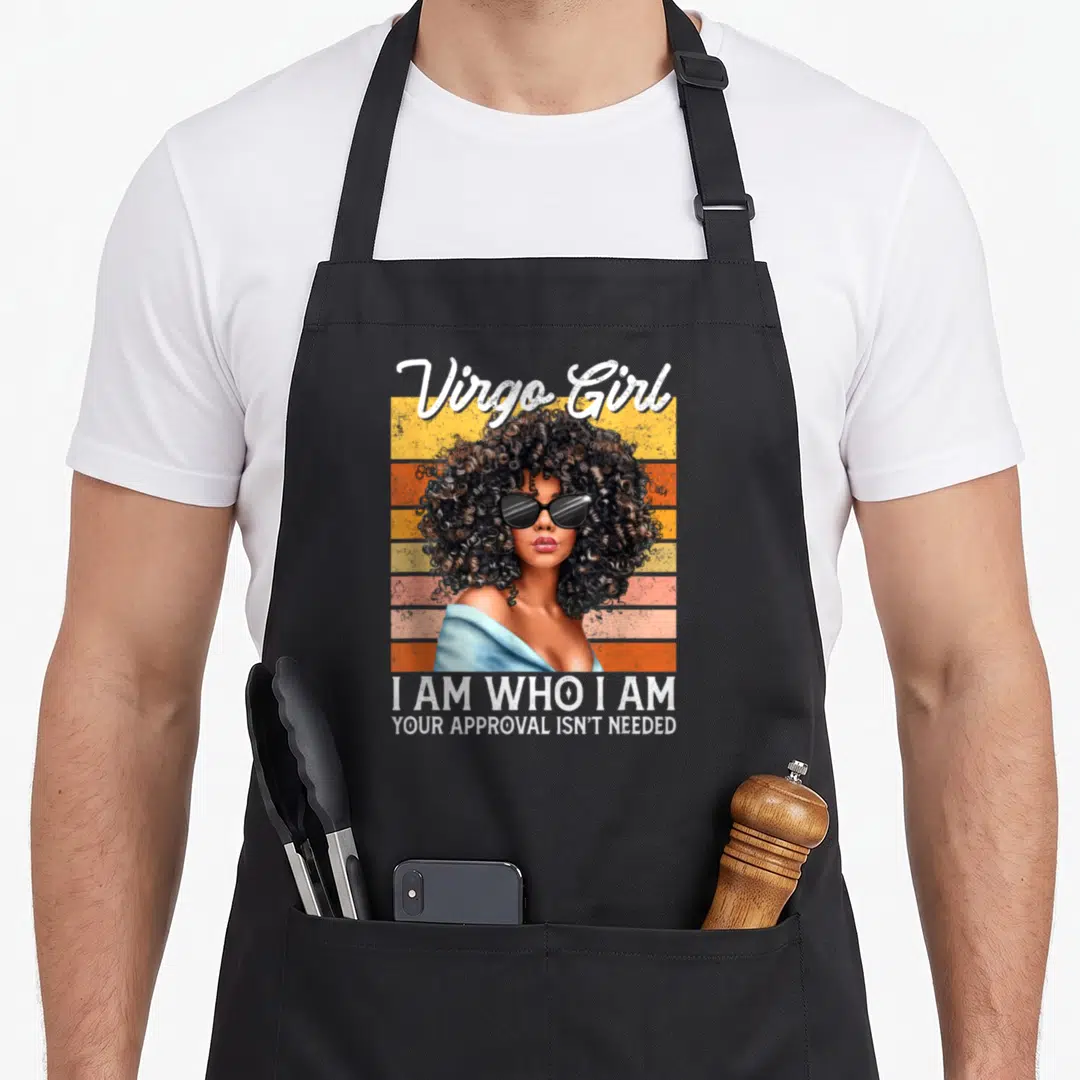 Virgo afro birthday apron - Woman with afro and sunglasses on retro stripes with text I AM WHO I AM YOUR APPROVAL ISN'T — shown on a black cotton canvas apron against a white background