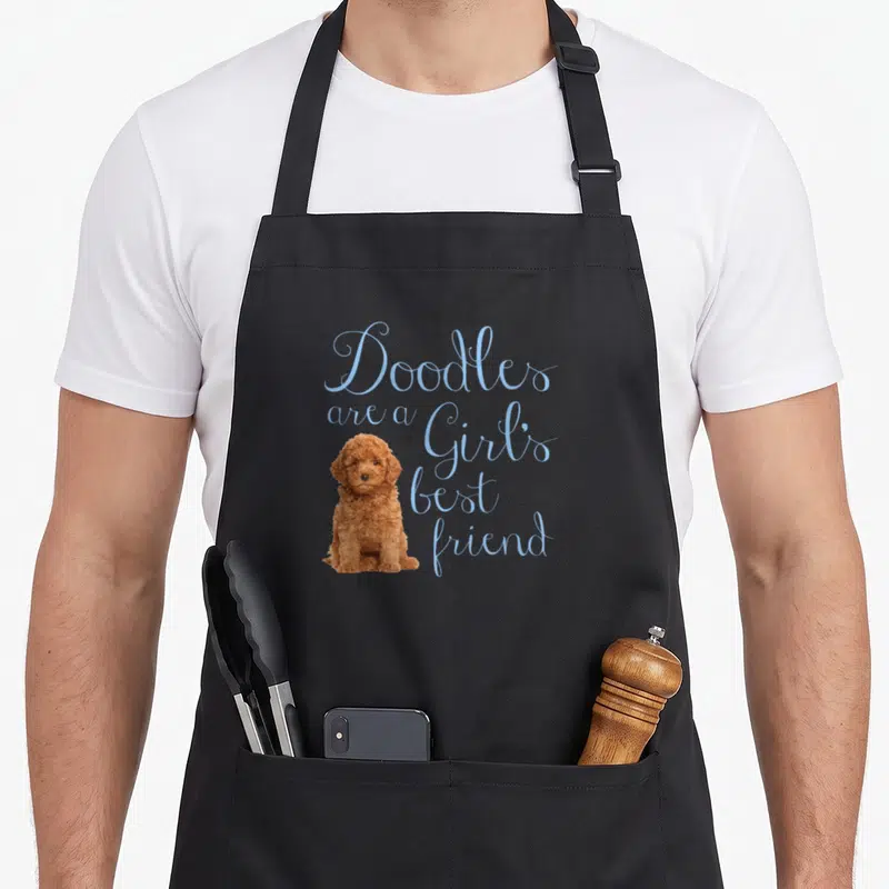 Doodle friend dog apron - Brown doodle sitting next to light blue script text reading Doodles are a Girl's best friend — shown on a black cotton canvas apron against a white background