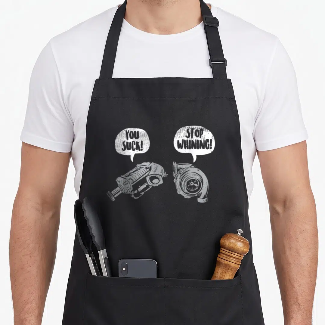 Suck racing apron - Two white turbochargers with speech bubbles reading YOU SUCK and STOP WHINING — shown on a black cotton canvas apron against a white background