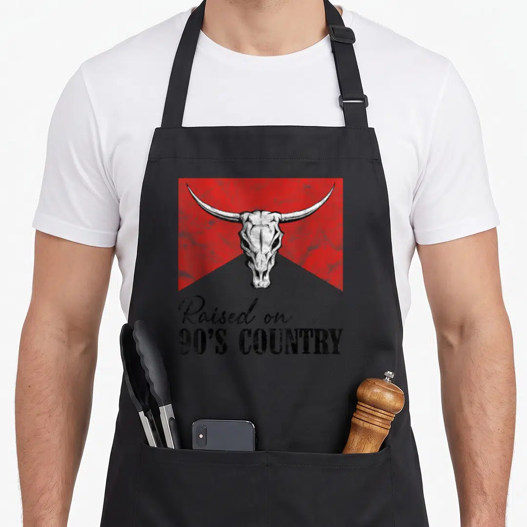 Bull country apron - White bull skull on red rectangle with black Raised on 90s Country text in distressed font — shown on a black cotton canvas apron against a white background