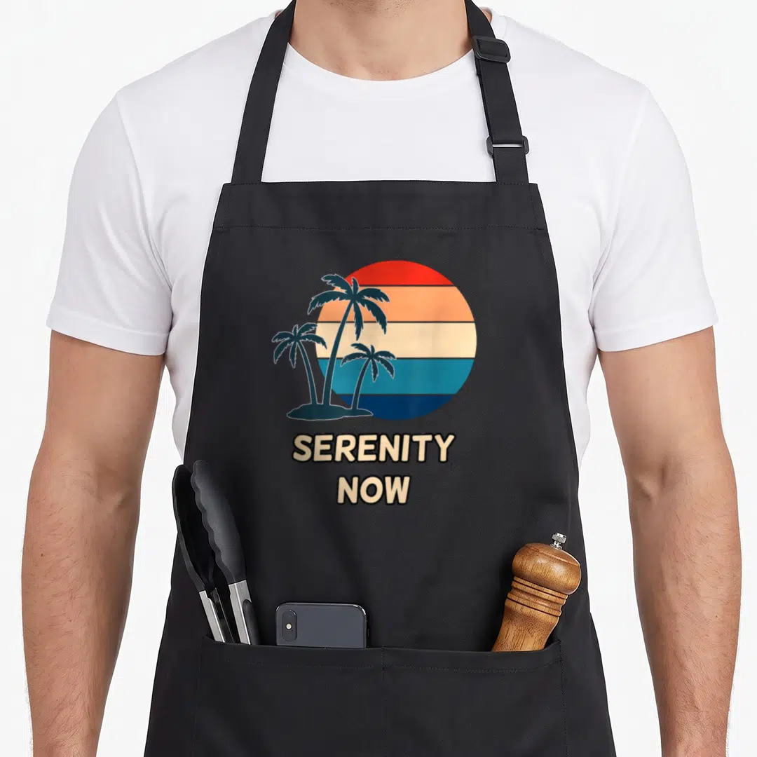 Fandom serenity apron - Retro striped sunset circle behind three blue palm trees with stacked SERENITY NOW text below — shown on a black cotton canvas apron against a white background