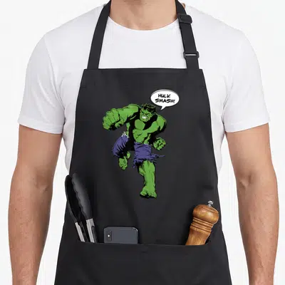 Smash hobby apron - Hulk in dynamic pose with speech bubble reading HULK SMASH! in green purple and white — shown on a black cotton canvas apron against a white background