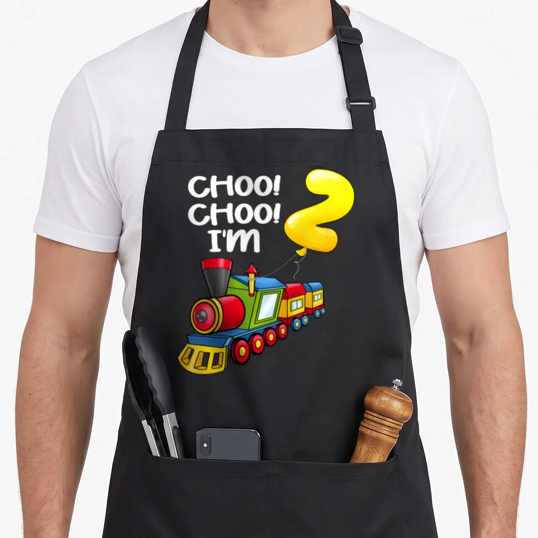 Choo 2nd apron - Cartoon train with yellow number two balloon and white text — shown on a black cotton canvas apron against a white background