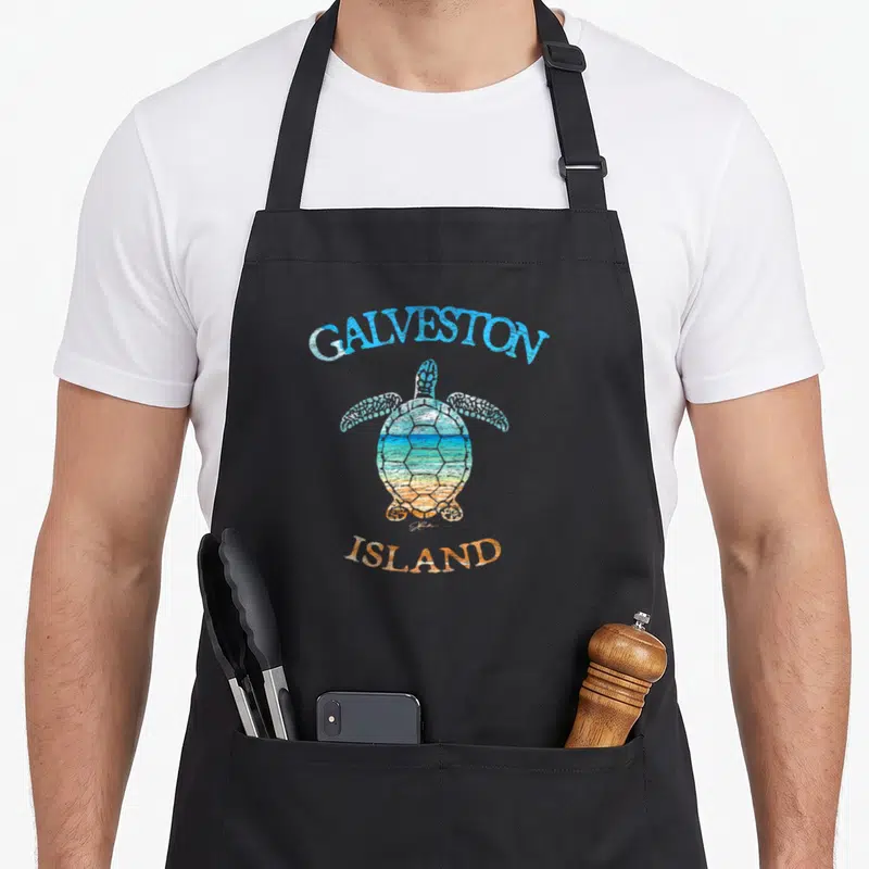 Sea galveston island apron - Sea turtle with beach scene in shell, arched GALVESTON ISLAND text in blue and orange — shown on a black cotton canvas apron against a white background