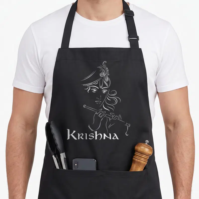 Hinduism diwali apron - White line art of Krishna playing flute above text Krishna on black background — shown on a black cotton canvas apron against a white background