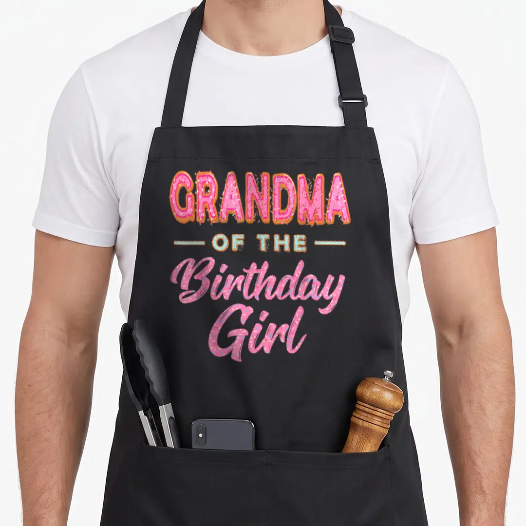 Donut grandma in apron - Pink and blue donut typography reading GRANDMA OF THE Birthday Girl with sprinkles — shown on a black cotton canvas apron against a white background