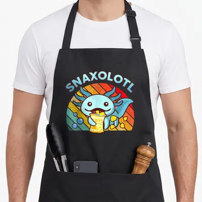 Axolotl food aprons - Cartoon blue axolotl holding yellow chip bag under arched SNAXOLOTL text against striped sunburst — shown on a black cotton canvas apron against a white background
