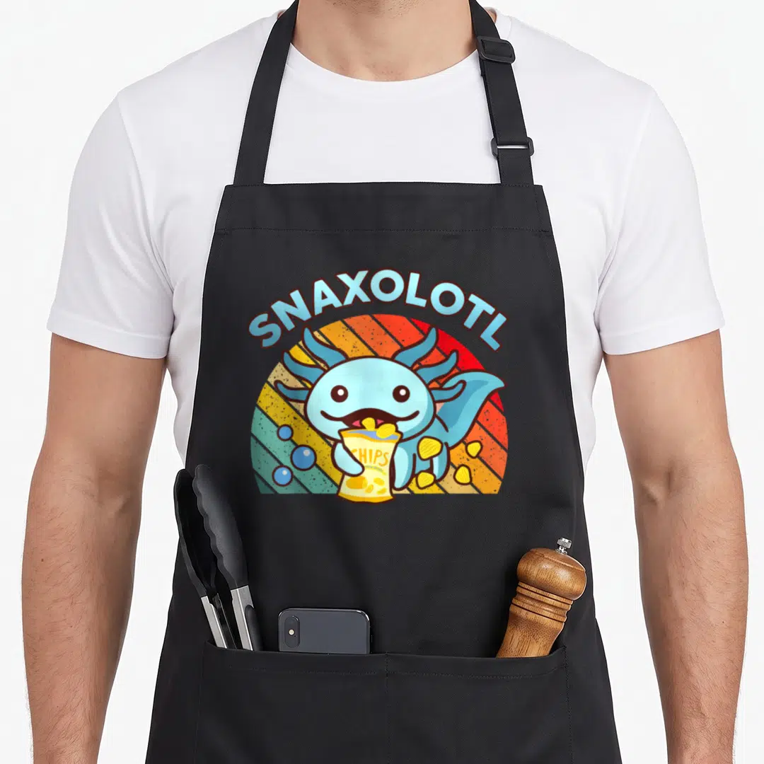 Axolotl food aprons - Cartoon blue axolotl holding yellow chip bag under arched SNAXOLOTL text against striped sunburst — shown on a black cotton canvas apron against a white background
