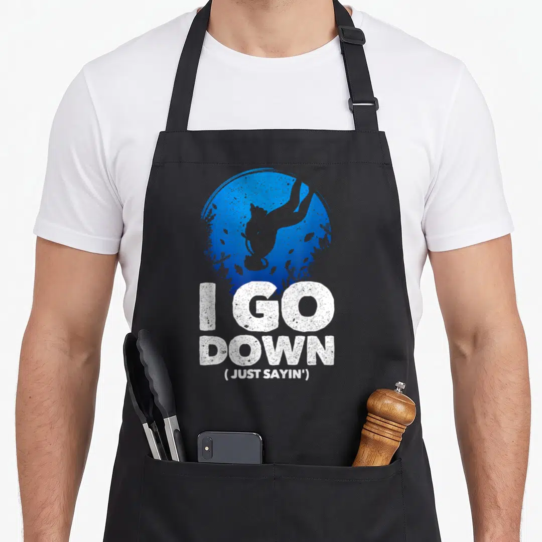 Funny diving lover apron - Blue circle with diver and coral above white I GO DOWN Just Sayin text — shown on a black cotton canvas apron against a white background