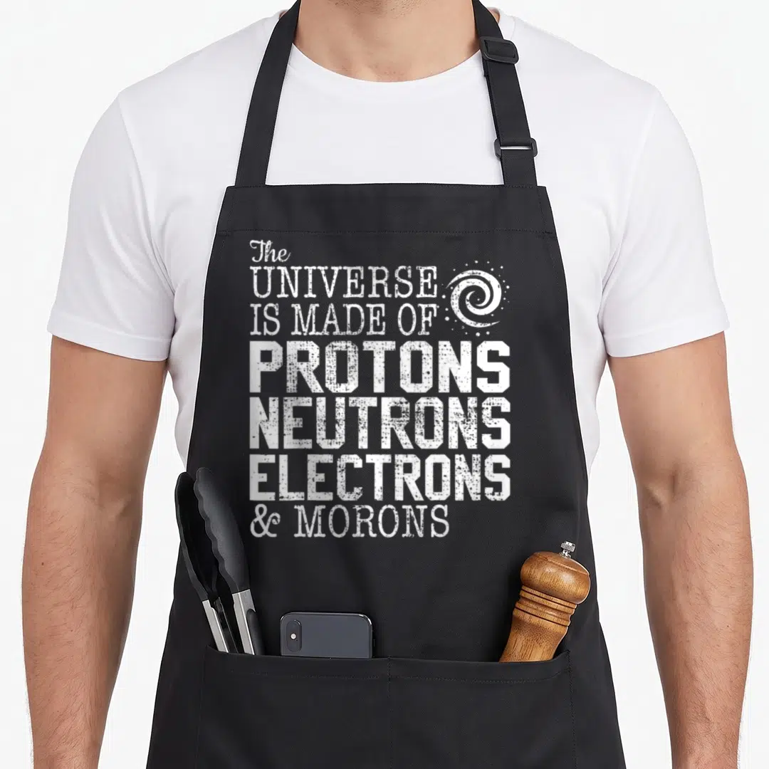 Science teacher chemistry apron - White distressed text reading universe made of protons neutrons electrons and morons — shown on a black cotton canvas apron against a white background
