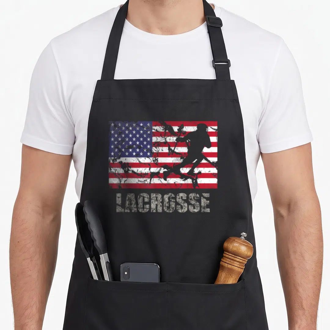 Lacrosse fan american flag apron - Distressed USA flag with grey lacrosse player silhouette and text below — shown on a black cotton canvas apron against a white background
