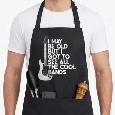 May but cooler apron - White electric guitar next to seven lines of distressed text reading I may be old but I got — shown on a black cotton canvas apron against a white background