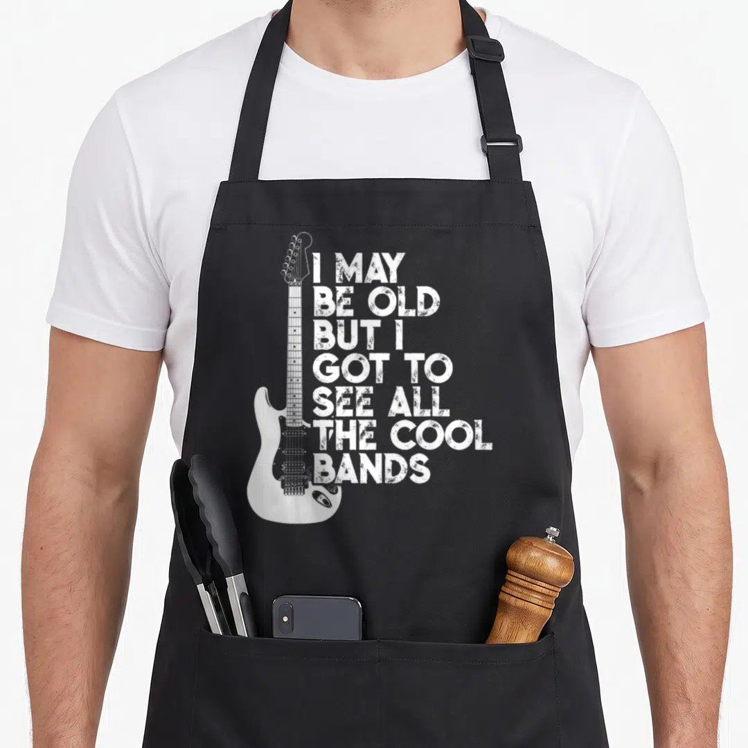 May but cooler apron - White electric guitar next to seven lines of distressed text reading I may be old but I got — shown on a black cotton canvas apron against a white background