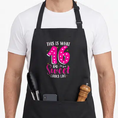 16th sweet birthday apron - Pink number 16 with white dots surrounded by text and yellow stars on black fabric — shown on a black cotton canvas apron against a white background
