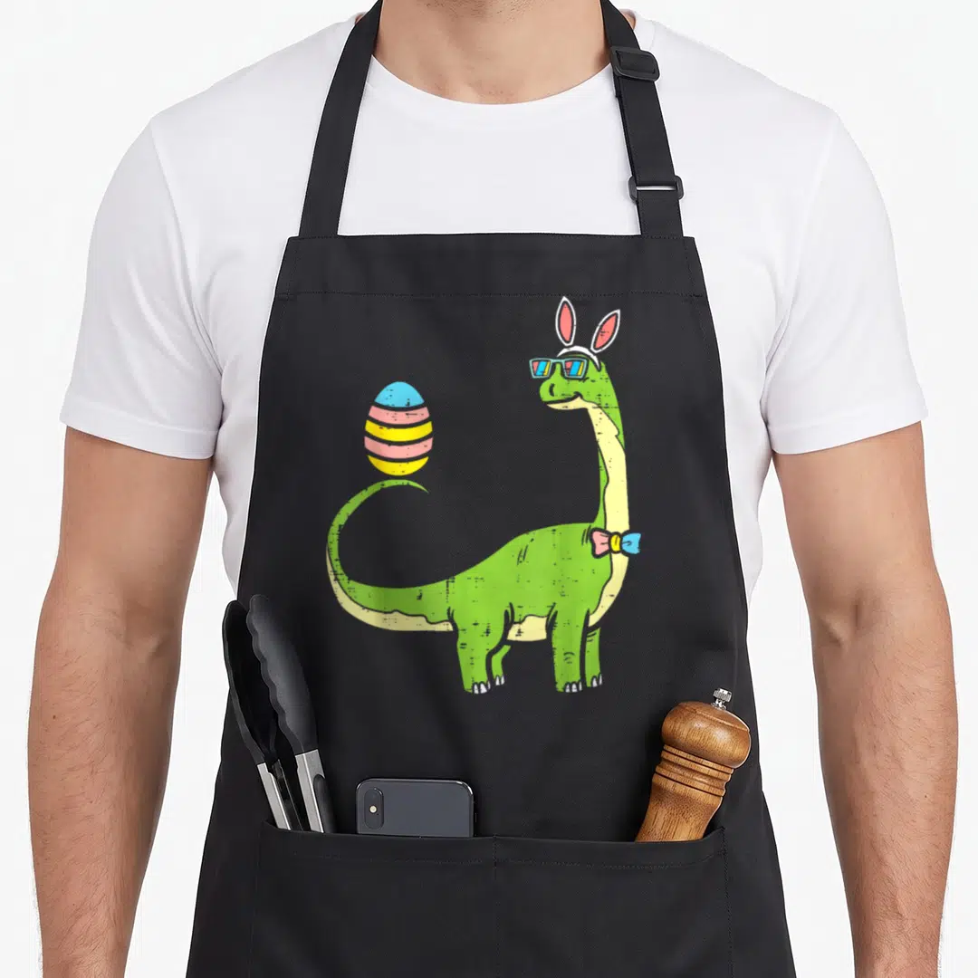 Brontosaurus easter bunny aprons - Green dinosaur with bunny ears, sunglasses, bowtie, and striped egg — shown on a black cotton canvas apron against a white background