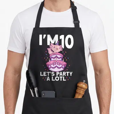 Axolotl 10th birthday apron - Pink axolotl in party hat on two tier cake with text I M 10 Lets Party A Lotl — shown on a black cotton canvas apron against a white background