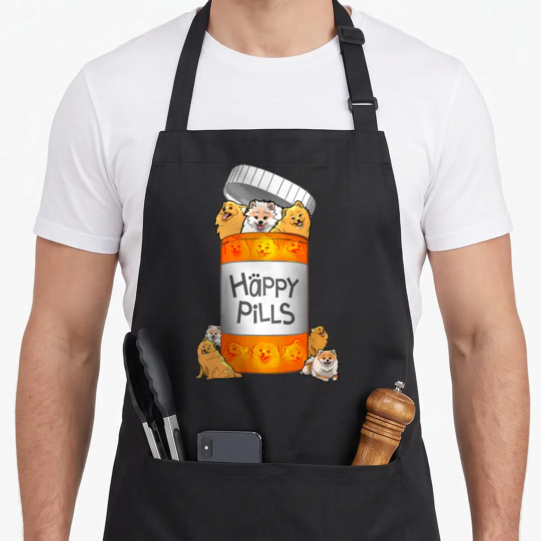 Pill pomeranian apron - Orange pill bottle with cartoon Pomeranians and Häppy PiLLS text on black fabric — shown on a black cotton canvas apron against a white background