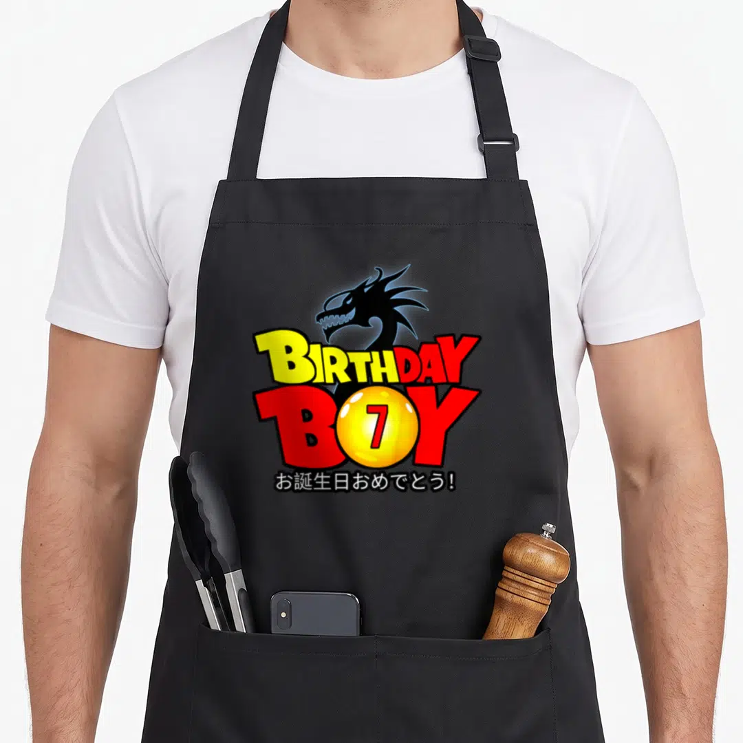 7th anime mom apron - Black dragon head above BIRTHDAY BOY text with yellow 7 sphere and Japanese greeting — shown on a black cotton canvas apron against a white background