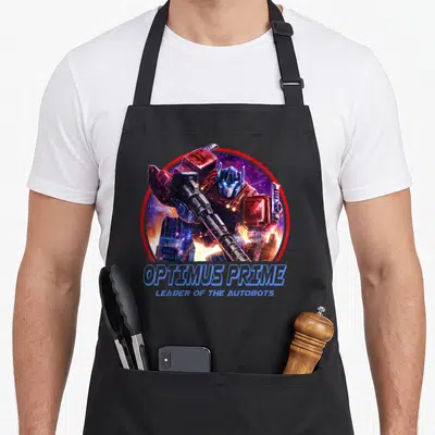 War transformer apron - Optimus Prime holding a gun in a red circle with blue text reading Leader of the Autobots — shown on a black cotton canvas apron against a white background