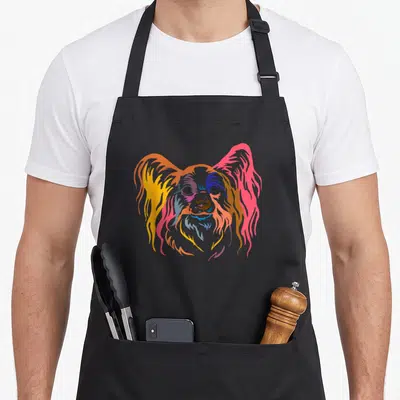 Cute papillon dog apron - Stylized colorful Papillon dog head in orange, yellow, pink, blue, and purple — shown on a black cotton canvas apron against a white background