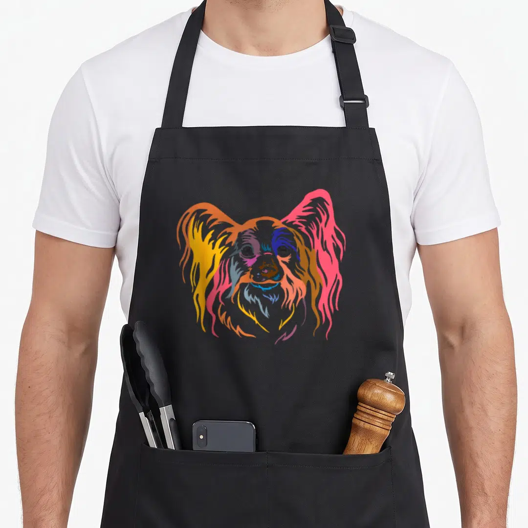 Cute papillon dog apron - Stylized colorful Papillon dog head in orange, yellow, pink, blue, and purple — shown on a black cotton canvas apron against a white background