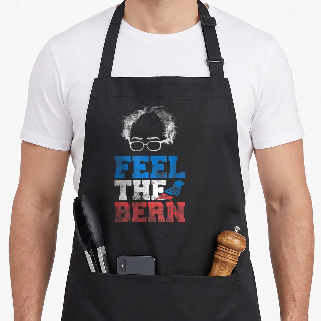 Bernie bird apron - Stylized head glasses FEEL THE BERN text blue white red distressed sparrow — shown on a black cotton canvas apron against a white background