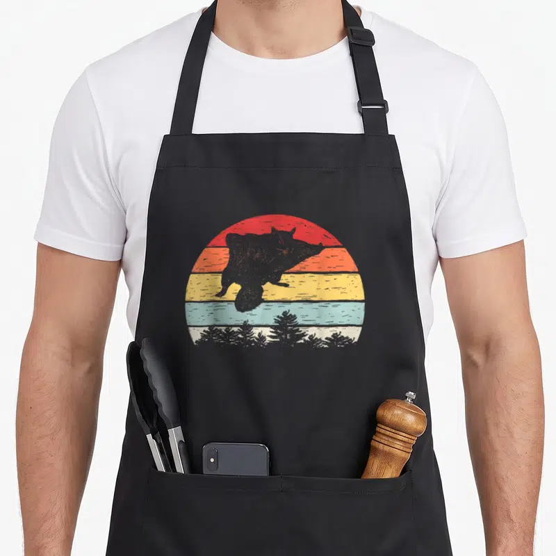 Catch flying apron - Grey squirrel silhouette over red orange yellow cream teal striped sun with pine trees — shown on a black cotton canvas apron against a white background