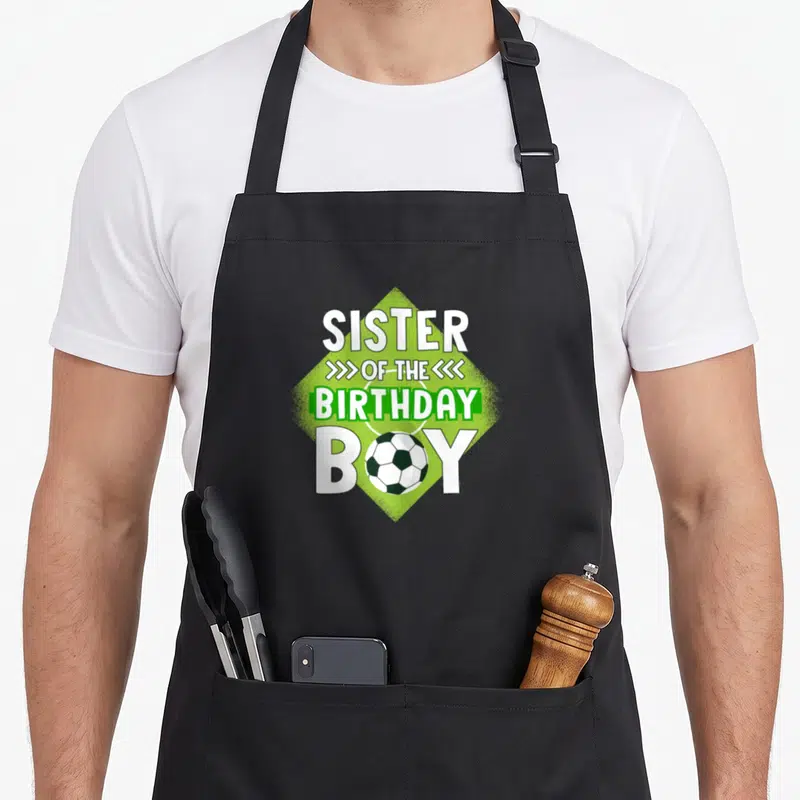 Sister soccer birthday apron - Stacked text Sister of the Birthday Boy with soccer ball replacing the O on a green — shown on a black cotton canvas apron against a white background