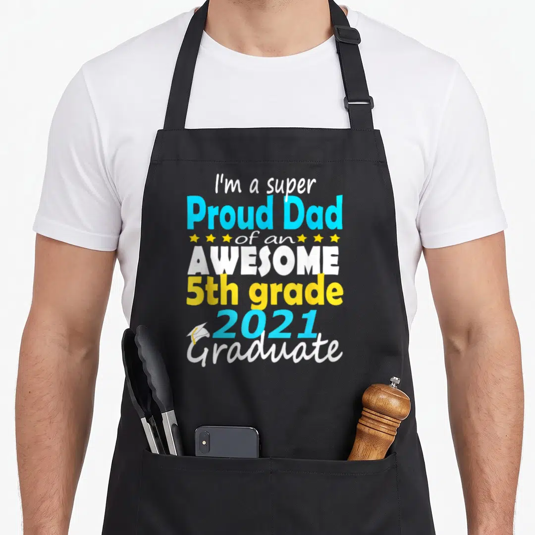 Proud grade boy apron - Stacked text I'm a super Proud Dad of an AWESOME 5th grade 2021 Graduate with stars and cap icon — shown on a black cotton canvas apron against a white background