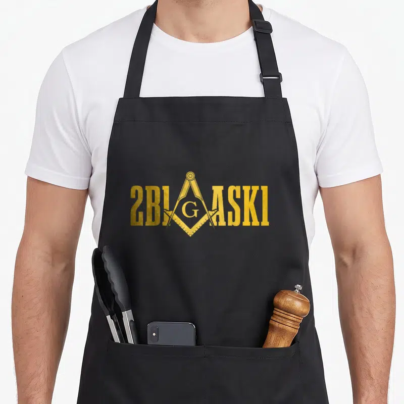 Freemason 2b1ask1 mason apron - Gold 2BIGASKI text with Masonic square compass G overlapping center — shown on a black cotton canvas apron against a white background