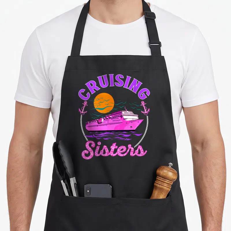 Sister cruising apron - Pink cruise ship under orange sun with anchors and Sisters text in rope circle — shown on a black cotton canvas apron against a white background