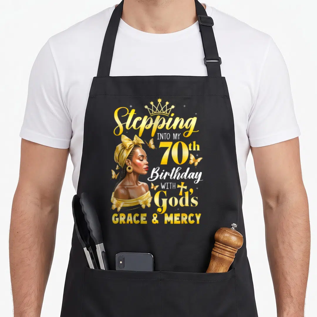 Afro 70th birthday apron - Woman profile with crown and butterflies next to Stepping Into My 70th Birthday With God's — shown on a black cotton canvas apron against a white background