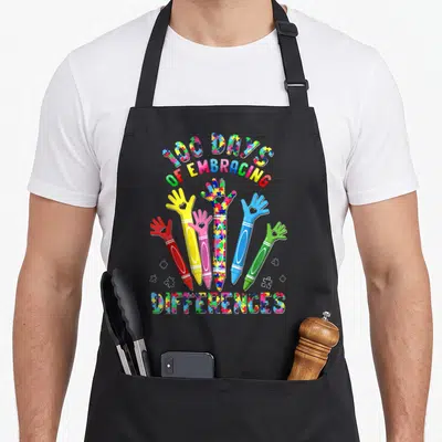 Autism iep apron - Six colorful crayon hands with puzzle piece patterns and text 100 Days of Embracing Differences — shown on a black cotton canvas apron against a white background