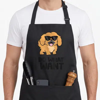Funny pekingese dog apron - Tan cartoon dog in black sunglasses with pink tongue above stacked black text reading I DO — shown on a black cotton canvas apron against a white background