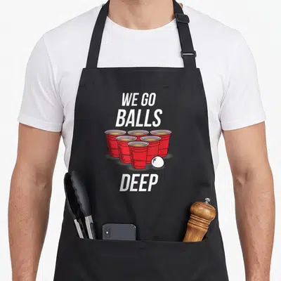 Ball beer pong apron - Six red cups and white ball with WE GO BALLS DEEP text — shown on a black cotton canvas apron against a white background