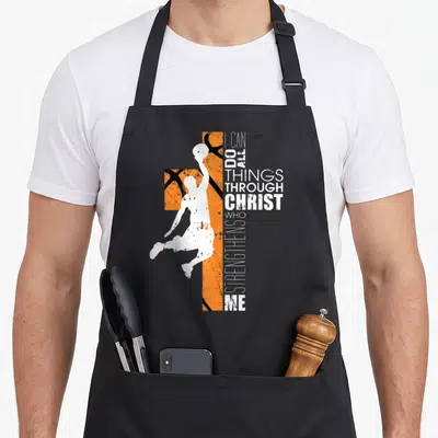 Basketball bible verse apron - White basketball player silhouette over orange textured cross with vertical I CAN DO ALL — shown on a black cotton canvas apron against a white background