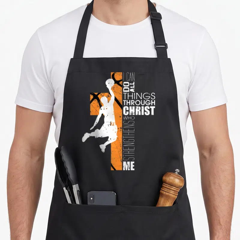 Basketball bible verse apron - White basketball player silhouette over orange textured cross with vertical I CAN DO ALL — shown on a black cotton canvas apron against a white background