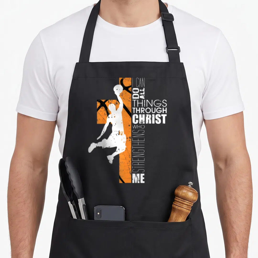 Basketball bible verse apron - White basketball player silhouette over orange textured cross with vertical I CAN DO ALL — shown on a black cotton canvas apron against a white background