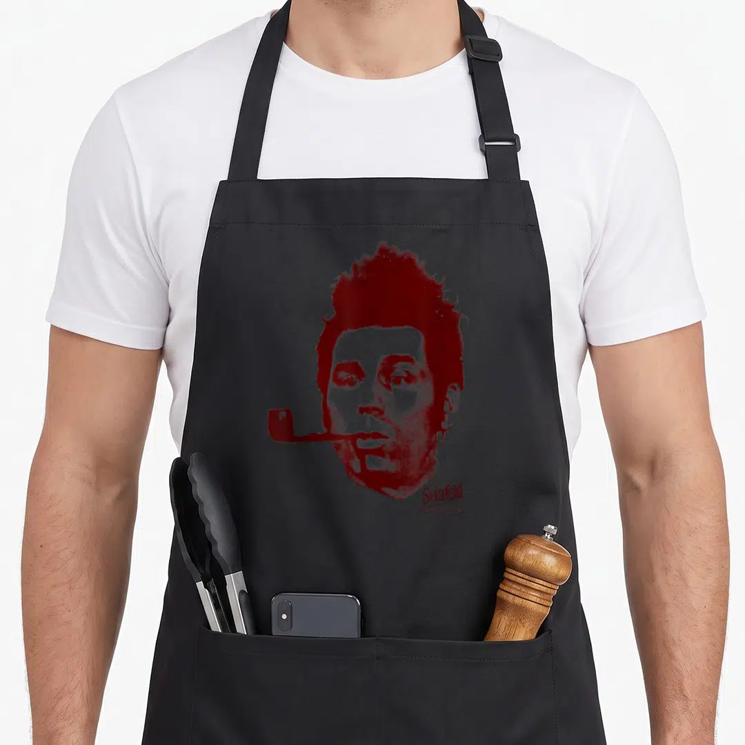 Kramer face apron - Distressed red portrait of a man with a pipe and Seinfeld text — shown on a black cotton canvas apron against a white background