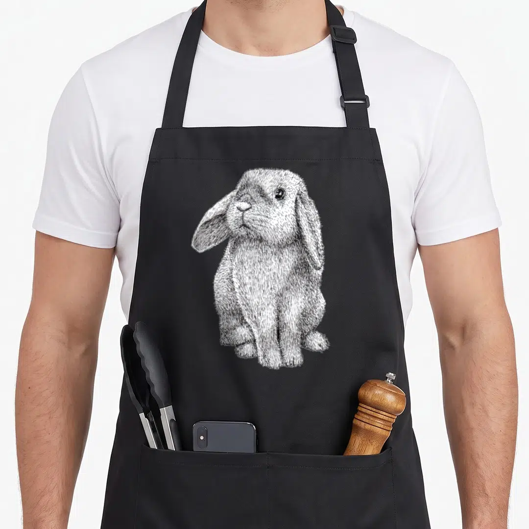 Lop eared bunny apron - Black and white line art of a sitting lop-eared rabbit with textured fur details — shown on a black cotton canvas apron against a white background