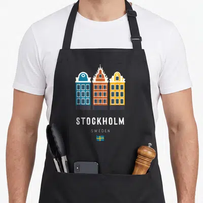 Stockholm scandinavian aprons - Three blue orange yellow buildings with Stockholm Sweden text and flag — shown on a black cotton canvas apron against a white background