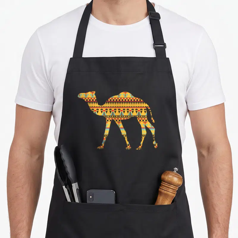 Middle camel apron - Camel silhouette filled with yellow orange blue red geometric patterns on black background — shown on a black cotton canvas apron against a white background