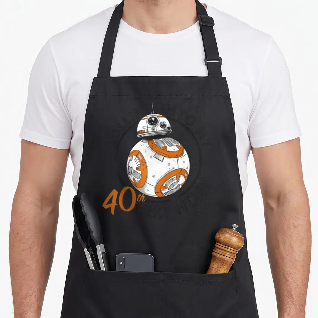 Rollin 40th birthday apron - BB-8 robot in grey circle with Rollin Into My 40th Birthday text — shown on a black cotton canvas apron against a white background