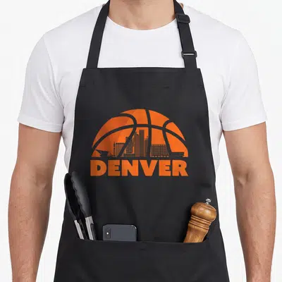 Skyline denver apron - Orange basketball graphic with integrated city skyline silhouette and DENVER text at the bottom — shown on a black cotton canvas apron against a white background